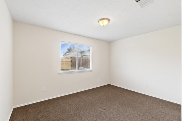 empty room featuring dark colored carpet, visible vents, and baseboards