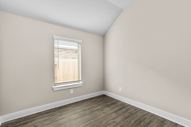 empty room featuring lofted ceiling, dark wood-style floors, and baseboards