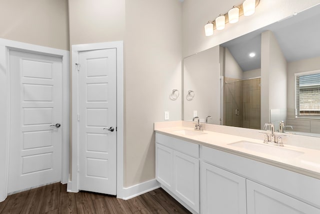 bathroom with double vanity, a shower stall, a sink, and wood finished floors