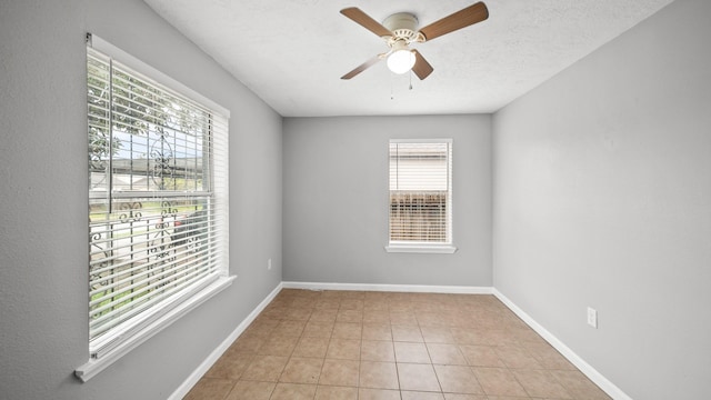 empty room featuring light tile patterned floors, a ceiling fan, baseboards, and a textured ceiling