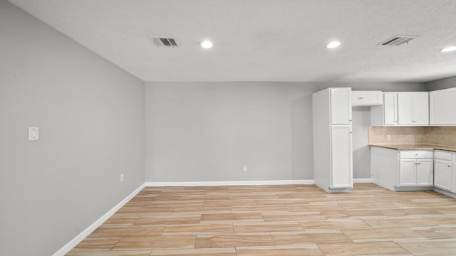 kitchen with white cabinetry, wood tiled floor, visible vents, and baseboards