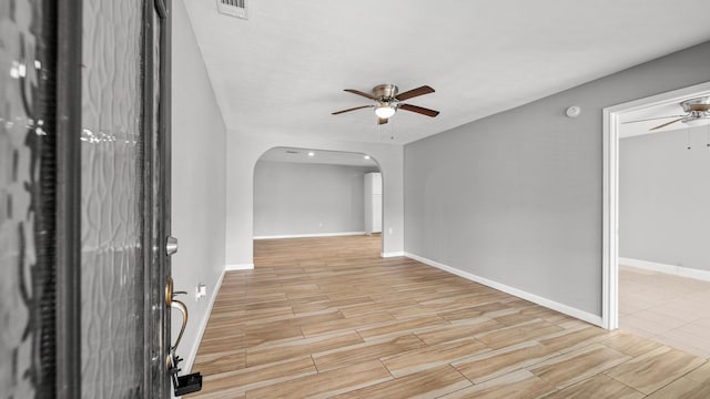 spare room with ceiling fan, arched walkways, wood finish floors, visible vents, and baseboards