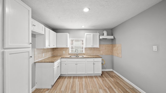 kitchen featuring light wood finished floors, backsplash, white cabinets, a sink, and baseboards