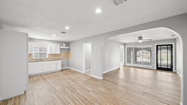 kitchen featuring tasteful backsplash, visible vents, open floor plan, white cabinetry, and a sink