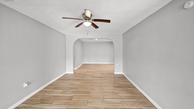 empty room featuring ceiling fan, arched walkways, baseboards, and wood finish floors