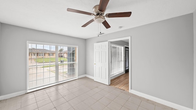 spare room featuring light tile patterned flooring, a ceiling fan, and baseboards