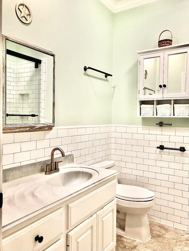 bathroom with toilet, vanity, tile walls, ornamental molding, and wainscoting