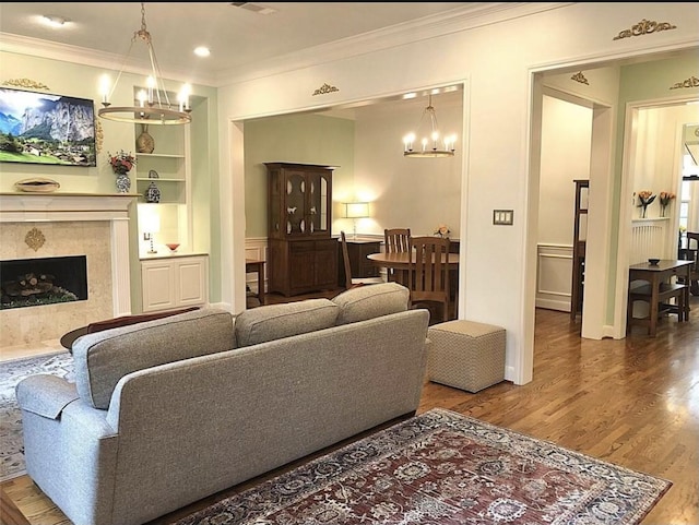 living room featuring crown molding, wood finished floors, built in features, and an inviting chandelier