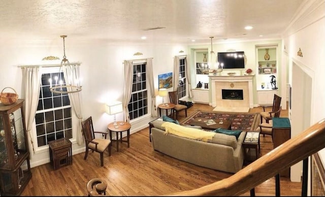 living area featuring a textured ceiling, a notable chandelier, a fireplace with flush hearth, wood finished floors, and ornamental molding