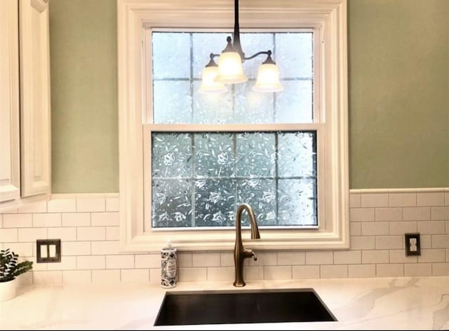 kitchen with hanging light fixtures, backsplash, a sink, and a wealth of natural light