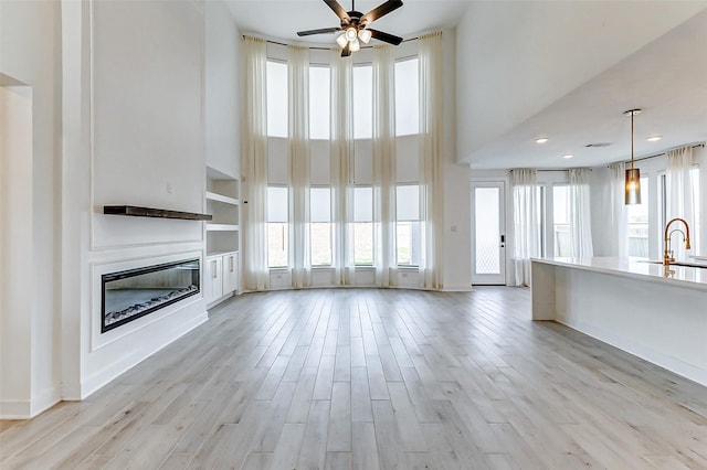 unfurnished living room featuring built in features, a high ceiling, a glass covered fireplace, a sink, and light wood-type flooring