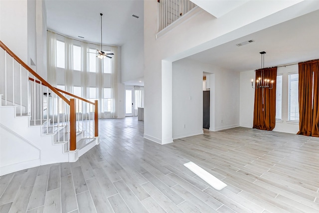 interior space with ceiling fan with notable chandelier, a high ceiling, visible vents, stairway, and light wood-type flooring