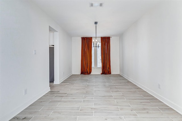 empty room featuring light wood-type flooring, visible vents, baseboards, and an inviting chandelier