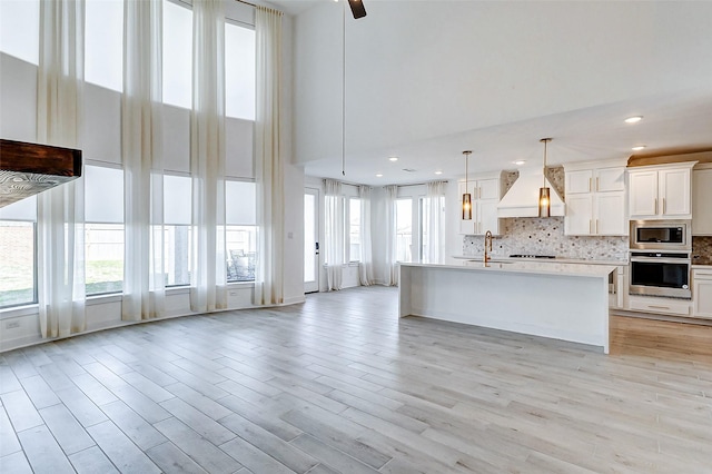 kitchen featuring custom exhaust hood, tasteful backsplash, light countertops, appliances with stainless steel finishes, and white cabinetry