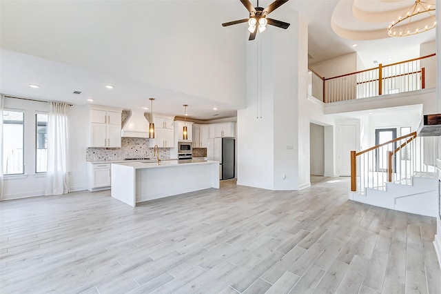 kitchen with custom range hood, appliances with stainless steel finishes, open floor plan, light countertops, and backsplash