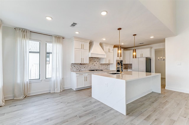 kitchen featuring custom exhaust hood, tasteful backsplash, visible vents, freestanding refrigerator, and gas cooktop