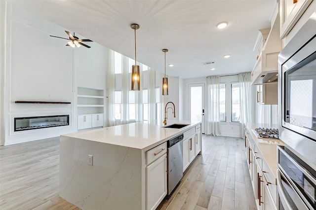 kitchen featuring light wood finished floors, appliances with stainless steel finishes, a sink, and a glass covered fireplace