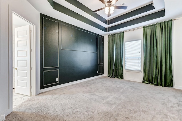 carpeted empty room with ceiling fan and a raised ceiling