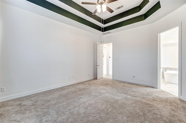 empty room featuring a tray ceiling, visible vents, a ceiling fan, carpet flooring, and baseboards