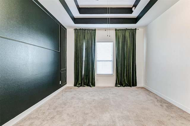 carpeted empty room featuring a tray ceiling, attic access, and baseboards