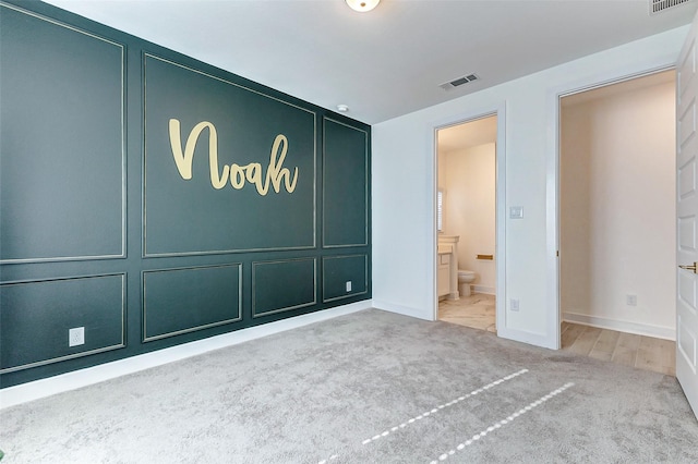 unfurnished bedroom featuring carpet flooring, a decorative wall, and visible vents