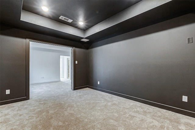 carpeted spare room featuring a tray ceiling, visible vents, baseboards, and recessed lighting