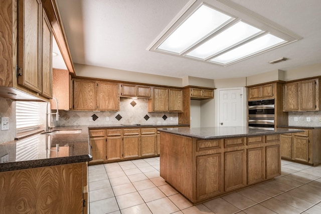 kitchen featuring light tile patterned floors, a skylight, a sink, tasteful backsplash, and brown cabinetry