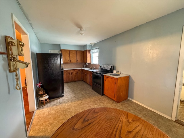 kitchen with electric range, brown cabinets, freestanding refrigerator, light countertops, and a sink