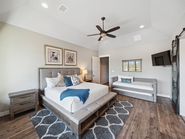 bedroom featuring vaulted ceiling, a barn door, wood finished floors, and visible vents