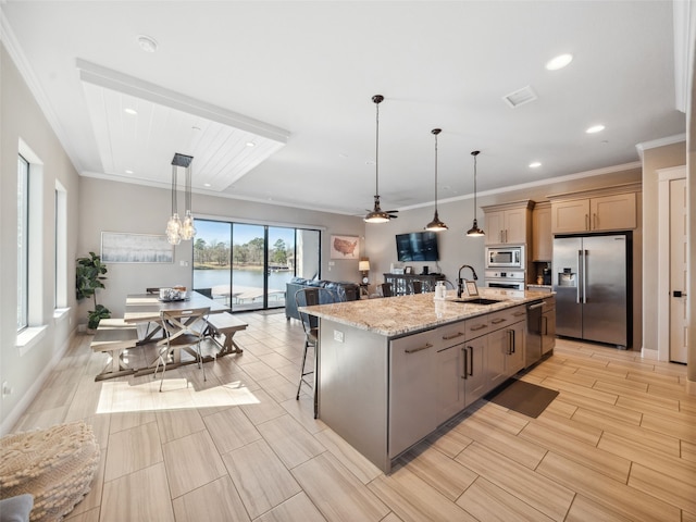 kitchen featuring light stone counters, hanging light fixtures, appliances with stainless steel finishes, a center island with sink, and crown molding