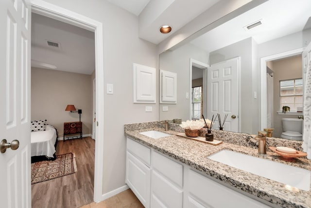 bathroom featuring wood finished floors, visible vents, a sink, and double vanity