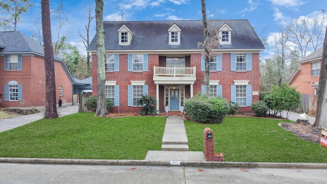 colonial house featuring brick siding, a front yard, fence, and a shingled roof