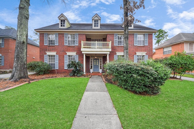 colonial house with brick siding, a front yard, and a balcony