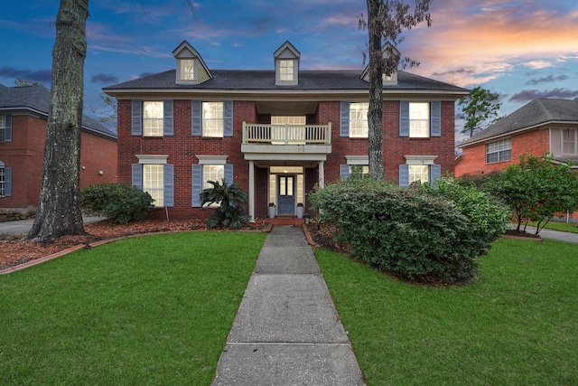 colonial inspired home featuring a balcony, brick siding, and a front yard