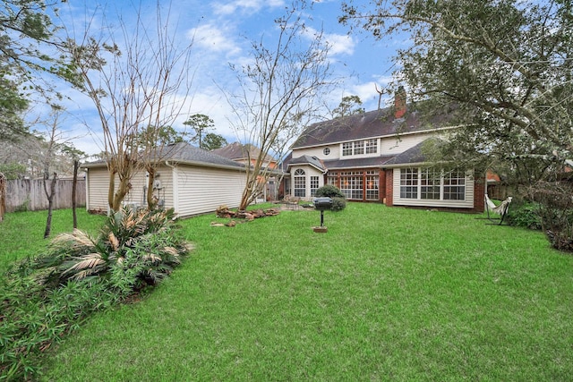 rear view of house with a chimney, fence, a lawn, and an outdoor structure