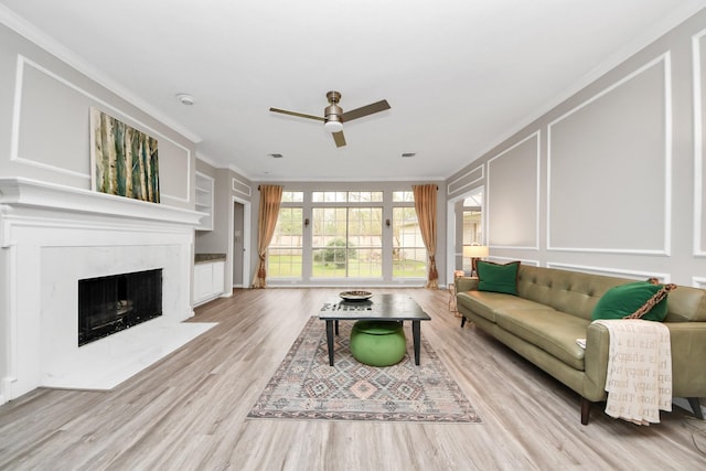 living room featuring crown molding, light wood-type flooring, a fireplace, and a decorative wall