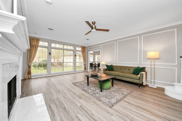 living room featuring a decorative wall, a fireplace, wood finished floors, visible vents, and crown molding