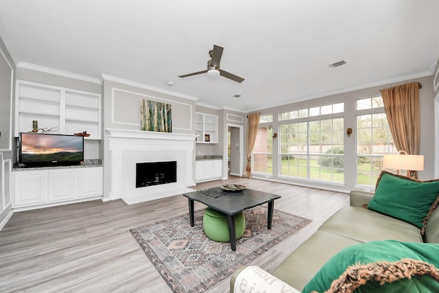 living room featuring built in shelves, a fireplace, wood finished floors, visible vents, and crown molding