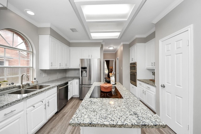 kitchen with stainless steel appliances, a sink, white cabinets, light wood-type flooring, and a center island