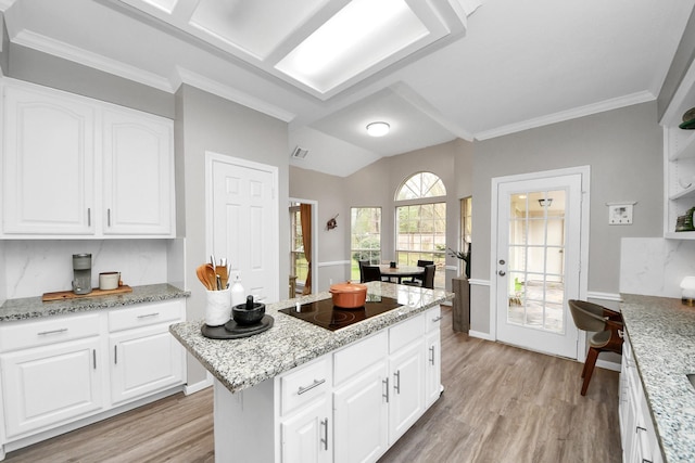 kitchen with light wood-style floors, white cabinetry, a kitchen island, light stone countertops, and black electric cooktop