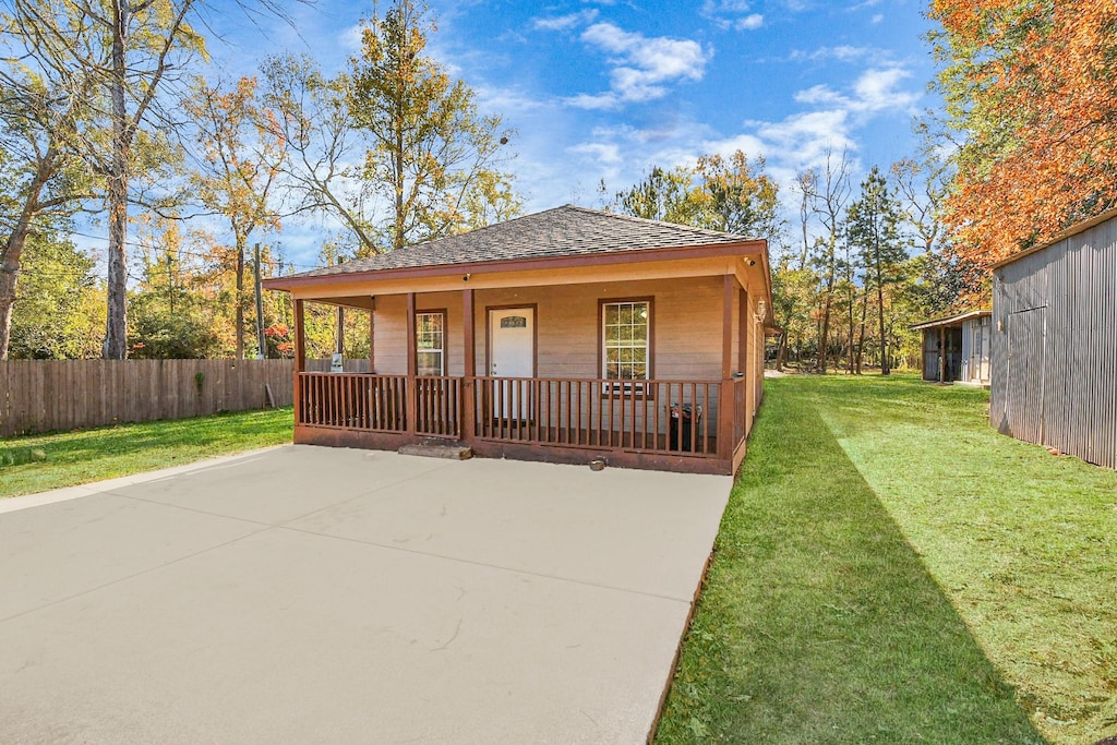 view of front of home featuring covered porch, a shingled roof, a front yard, and fence