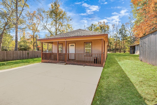 view of front of home featuring covered porch, a shingled roof, a front yard, and fence