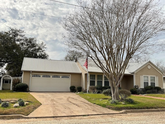 single story home with a garage, a front lawn, metal roof, and concrete driveway