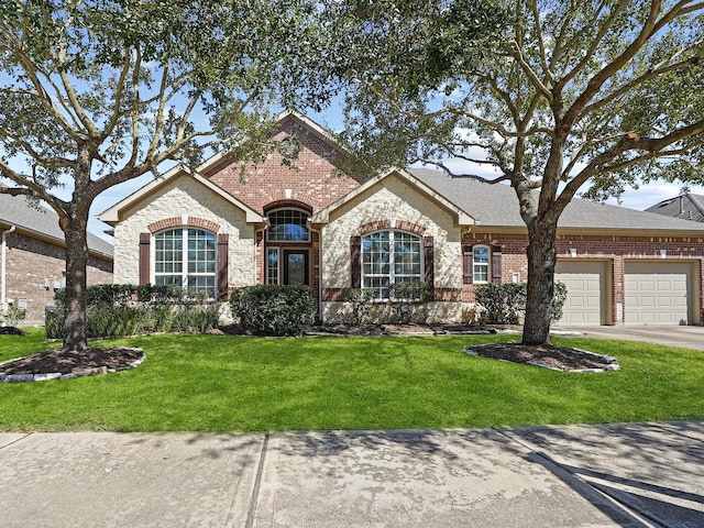 view of front of home with an attached garage, brick siding, driveway, stone siding, and a front yard