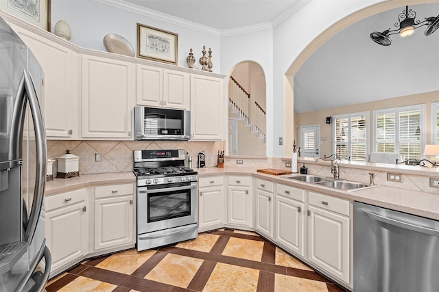 kitchen featuring appliances with stainless steel finishes, decorative backsplash, a sink, and ornamental molding