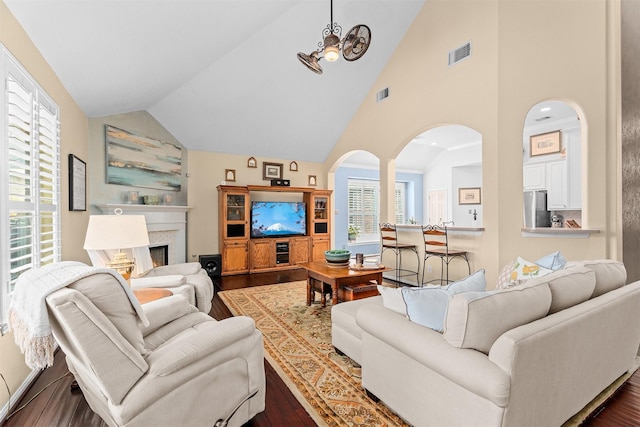 living area with high vaulted ceiling, a high end fireplace, visible vents, and dark wood finished floors