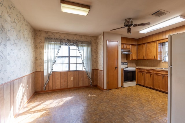 kitchen with plenty of natural light, white appliances, wainscoting, and wallpapered walls