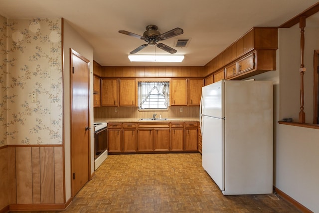 kitchen with visible vents, brown cabinetry, wainscoting, a sink, and white appliances