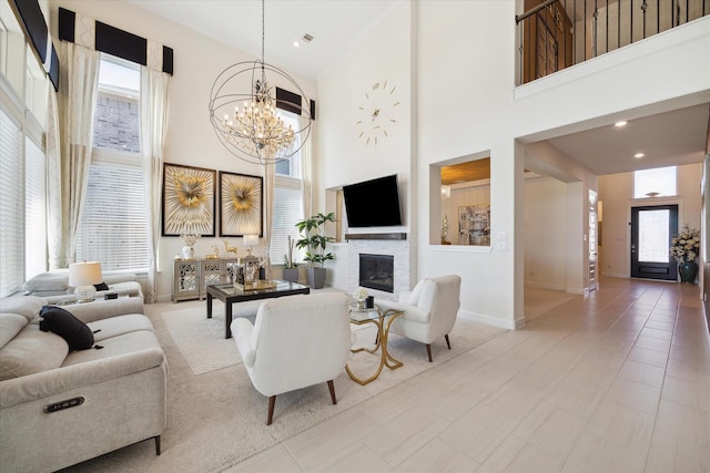 living area with recessed lighting, a towering ceiling, baseboards, a glass covered fireplace, and an inviting chandelier