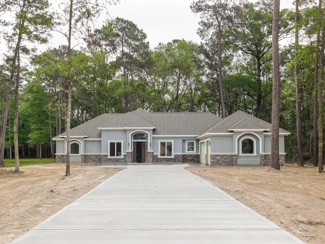 view of front facade with stone siding, roof with shingles, concrete driveway, and stucco siding